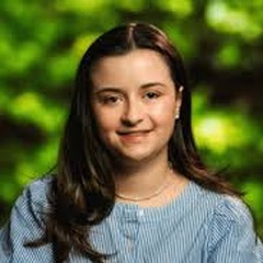 Portrait of Christina Charie in a blue striped blouse in front of green foliage.