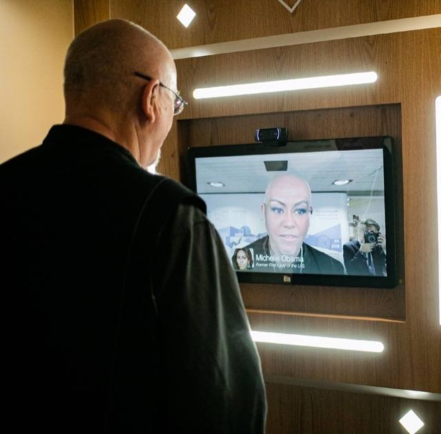 A man watches a screen showing a live deepfake that has replaced his own face with Michelle Obama&rsquo;s.