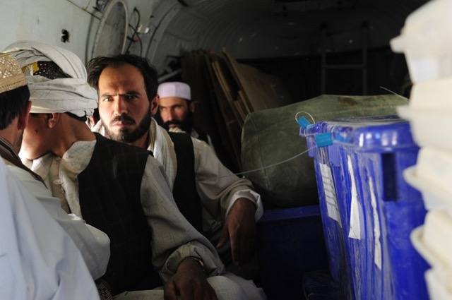 Afghan election officials seated beside sealed ballot boxes and portable voting booths inside a helicopter.