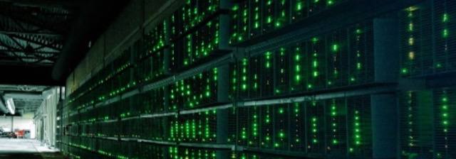 Racks of cryptocurrency mining computers glowing green in a dark warehouse.
