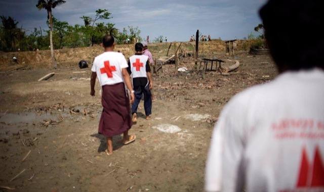 Aid workers in Red Cross vests walk through a storm-damaged village.