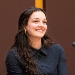Portrait of Charlotte Roberts smiling while seated at a panel discussion.
